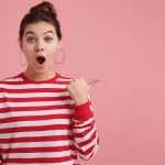 amazed young female with freckles wears striped longsleeve openes mouth widely excitement dropped jaw draws attention isolated pink wall
