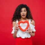 surprised black woman with heart shape isolated red