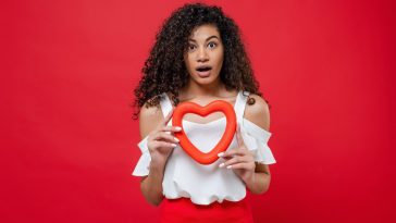 surprised black woman with heart shape isolated red